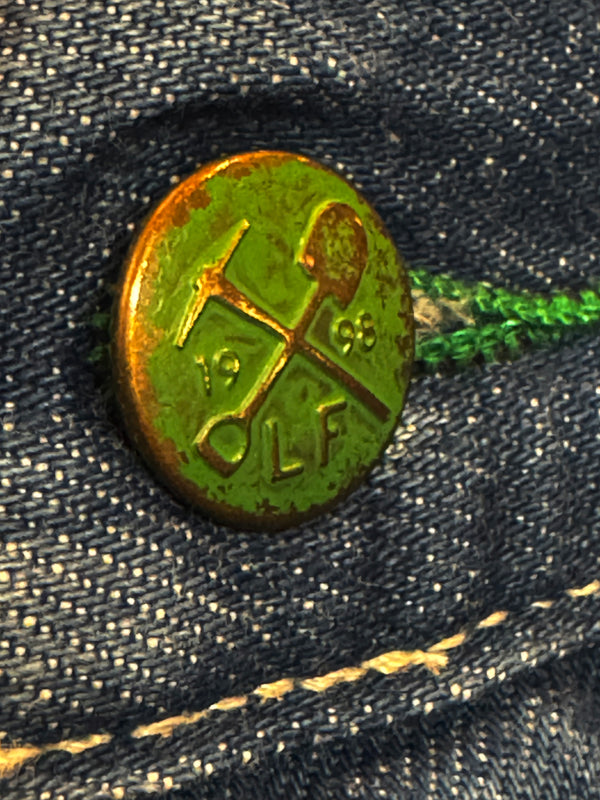 Green metal pin with symbols and text on a denim background