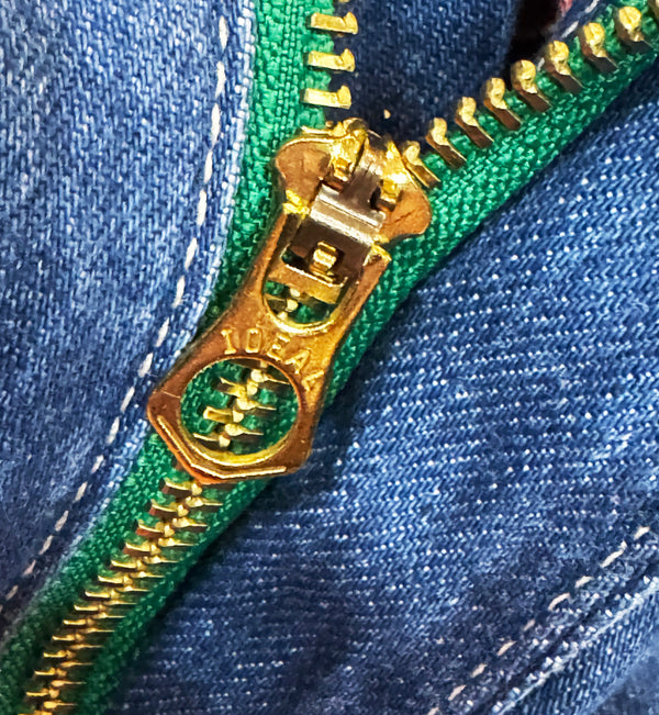 Close-up of a gold zipper pull on a green zipper against a blue denim background.