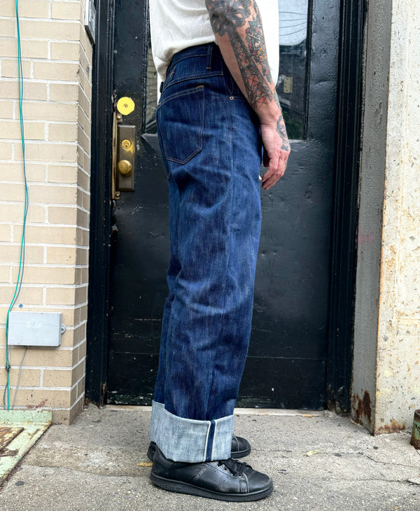 Person wearing blue jeans and black shoes standing in front of a door.