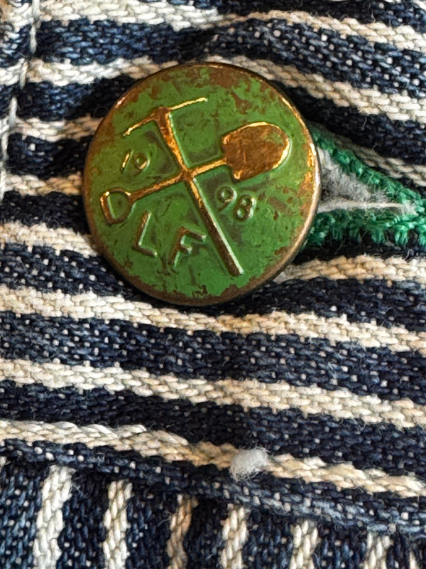 Green and gold pin on a striped fabric background