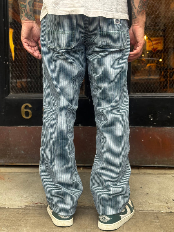 Person wearing hickory striped pants standing on a sidewalk 
