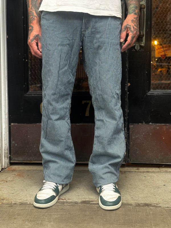 Person wearing hickory stripe pants and white sneakers standing in front of a door.