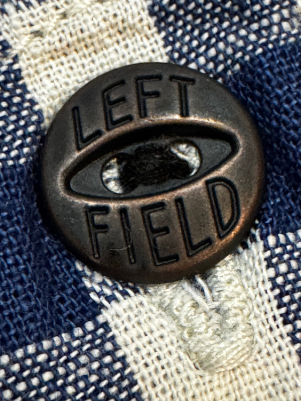 Close-up of a button with 'Left Field' branding on a checkered fabric background
