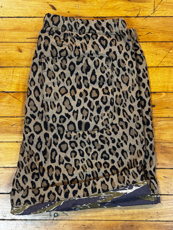 A leopard print skirt laid flat on a wooden floor. The skirt features a classic leopard pattern with black and dark brown spots on a tan base, and a solid dark navy blue inner lining visible along the right edge.
