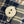 A close-up of a single round white button with two holes, placed on a navy, beige, and brown plaid fabric background.