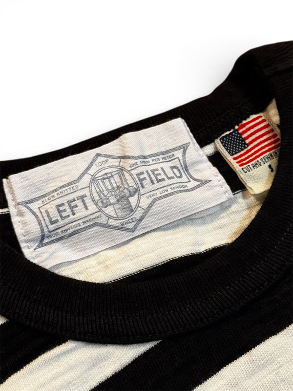 Close-up of a Left Field label on a black and white striped shirt with an American flag patch.