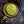 A close-up of a round vintage button or badge with a green background and crossed shovel and pickaxe symbols, set against a dark textured fabric.