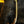 A close-up of a curved, antique brass-colored metal hook or clasp with a serrated edge, resting against a textured black fabric background.