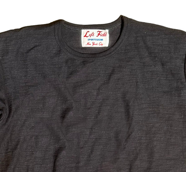 A black crew neck t-shirt with a tag visible at the neckline, laid flat on a plain surface.