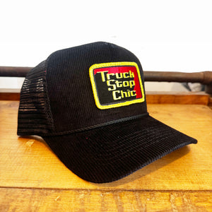 Black trucker hat with 'Truck Stop Chic' logo on a wooden surface