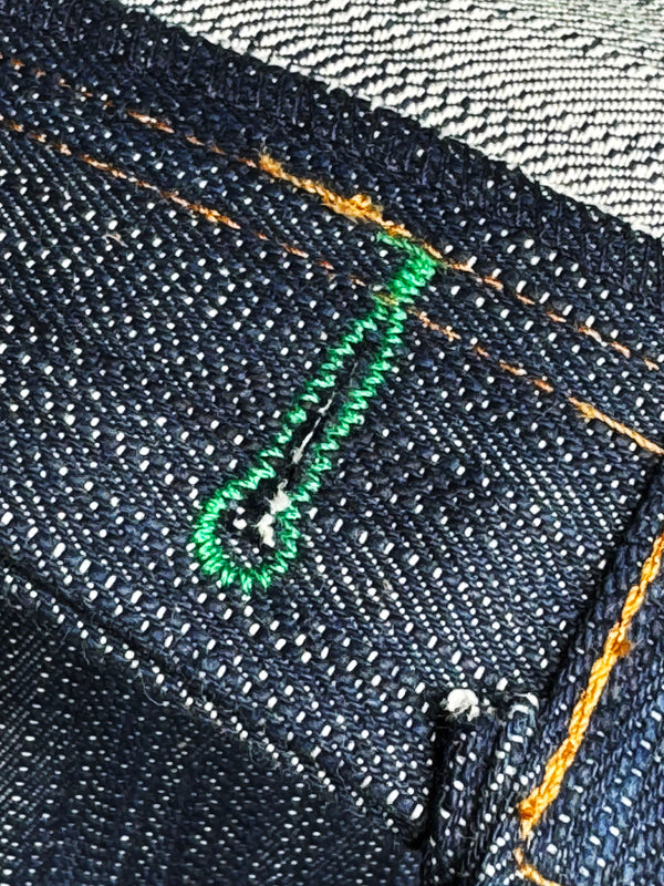 Close-up of dark denim fabric with green thread stitching