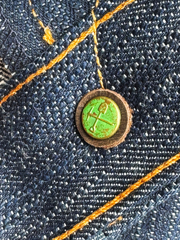 Close-up of a green button with a design on blue denim fabric.