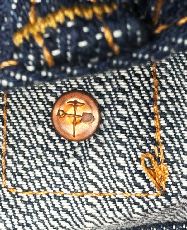 Close-up of a button on denim fabric with gold stitching.