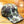 A baseball cap with a classic camouflage pattern in shades of green, brown, and beige, resting on a wooden plank floor.
