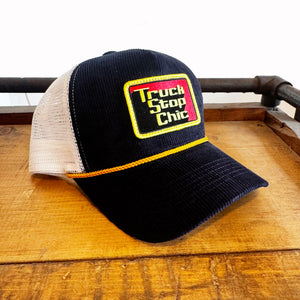 Black and white cap with 'Truck Stop Chic' logo on a wooden surface