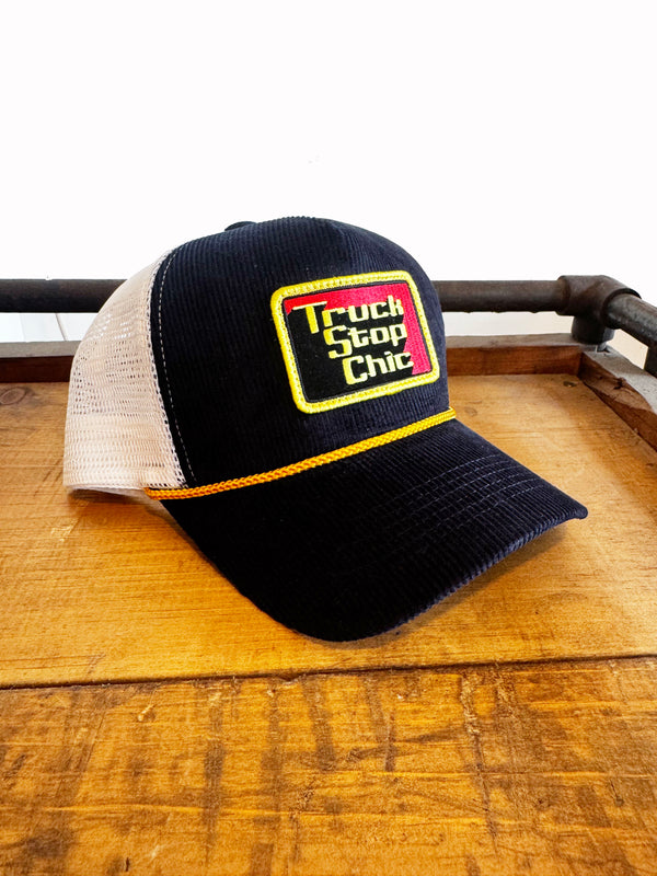 Black and white cap with 'Truck Stop Chic' logo on a wooden surface
