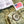 Close-up of olive green denim fabric showing a white woven label with black text, a small American flag patch, and a gray metal button.