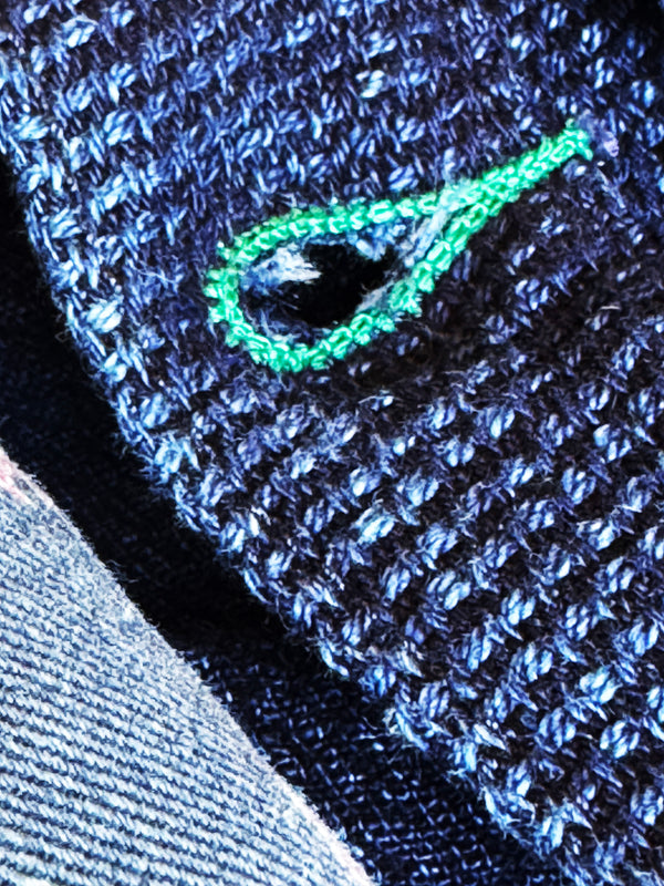 Close-up of a blue textured fabric with a green embroidered design.