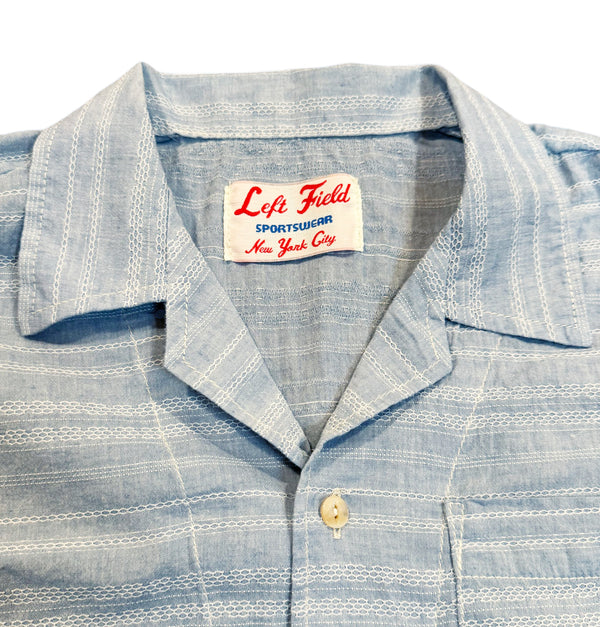 A pale blue short-sleeved camp shirt with Trocus pearl buttons and a collar, displayed against a white background.