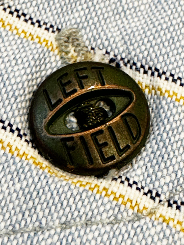 Bronze button with 'LEFT FIELD' text on a denim fabric background