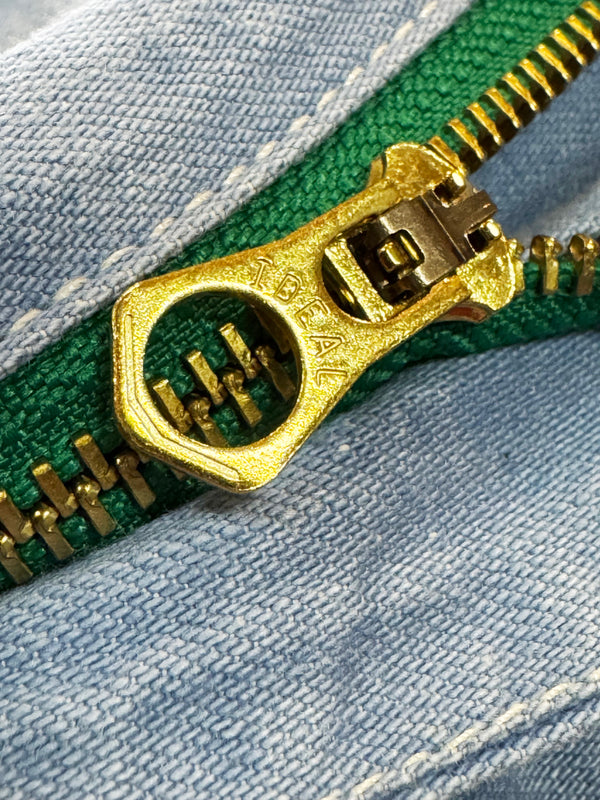Close-up of a gold zipper pull on green fabric with a blue denim background