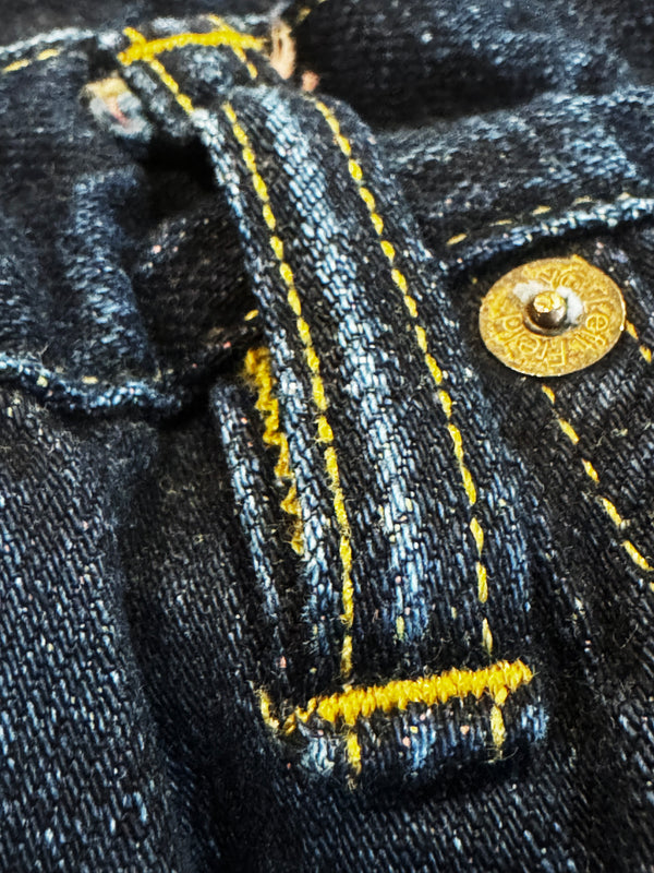 Close-up of black denim fabric with yellow stitching and a gold button.