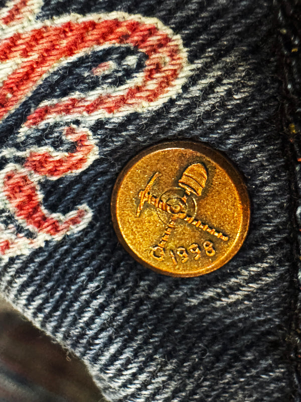 Close-up of a gold coin with '1998' on denim fabric with embroidered lettering.