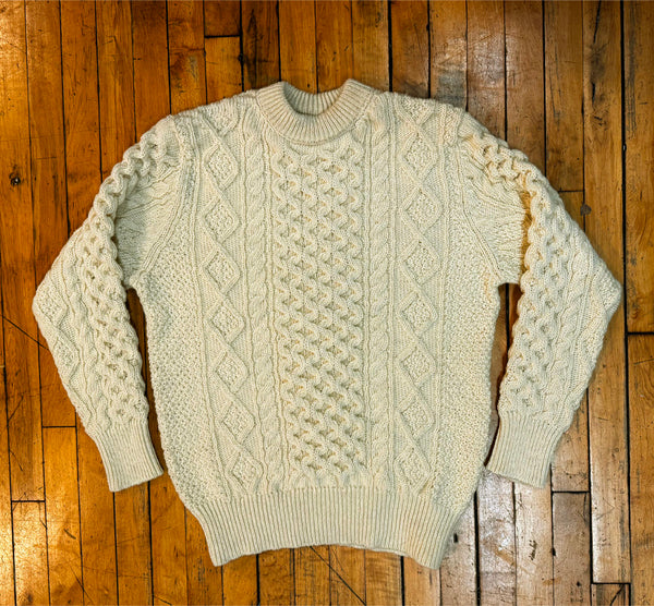 Cream-colored cable knit sweater on a wooden floor
