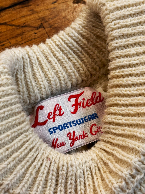 Close-up of a beige knitted sweater with a 'Left Field Sportswear New York City' label.