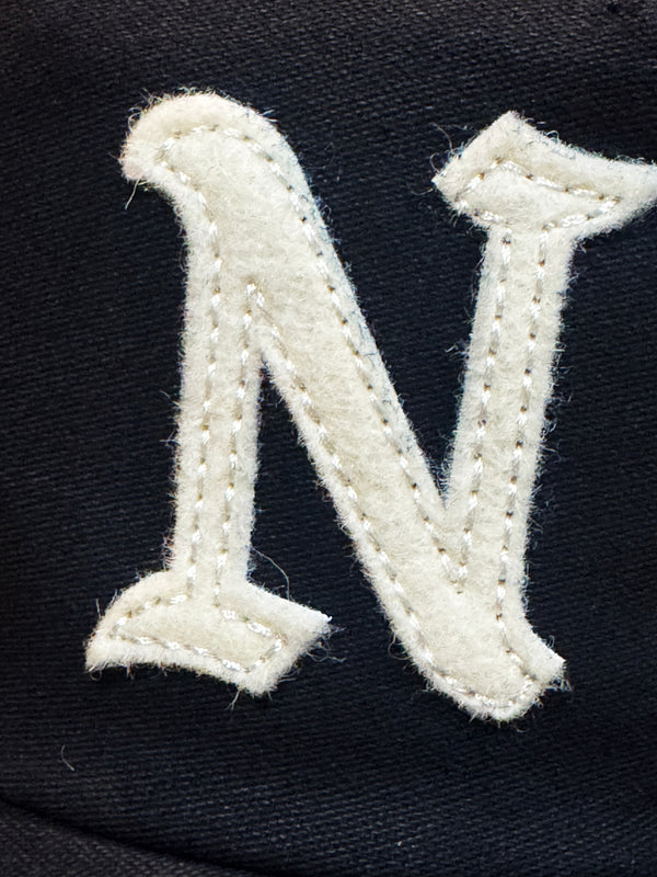 A close-up of a cream-colored embroidered letter 'N' on a black fabric surface.
