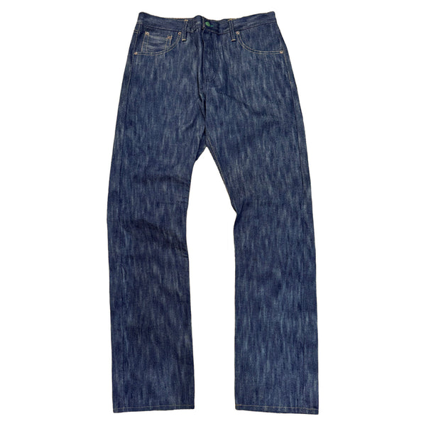 A pair of blue denim jeans laid flat, showcasing the natural plant dyed Indigo pattern and green selvedge.