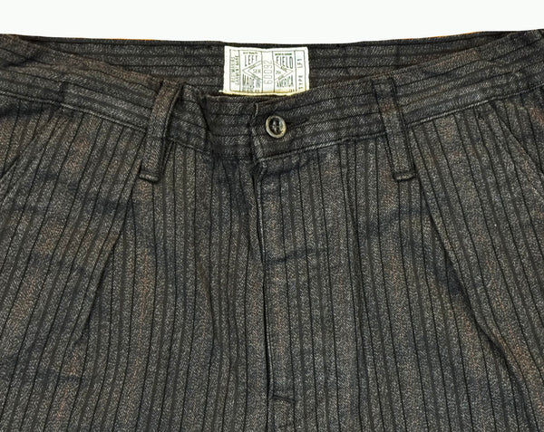 Close-up of gray pleated pants with a brand label on a white background